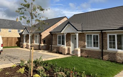 two newly built bungalows with light bricks and slate roofs. They have a small garden and driveway.