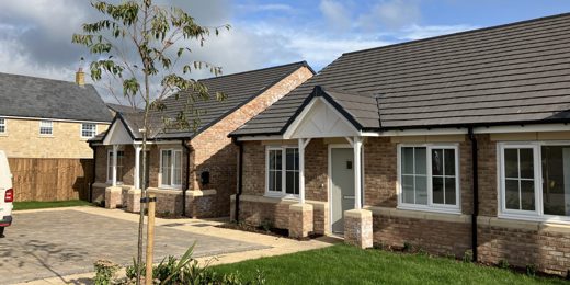 two newly built bungalows with light bricks and slate roofs. They have a small garden and driveway.