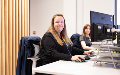 A person sat at a desk smiling towards the camera