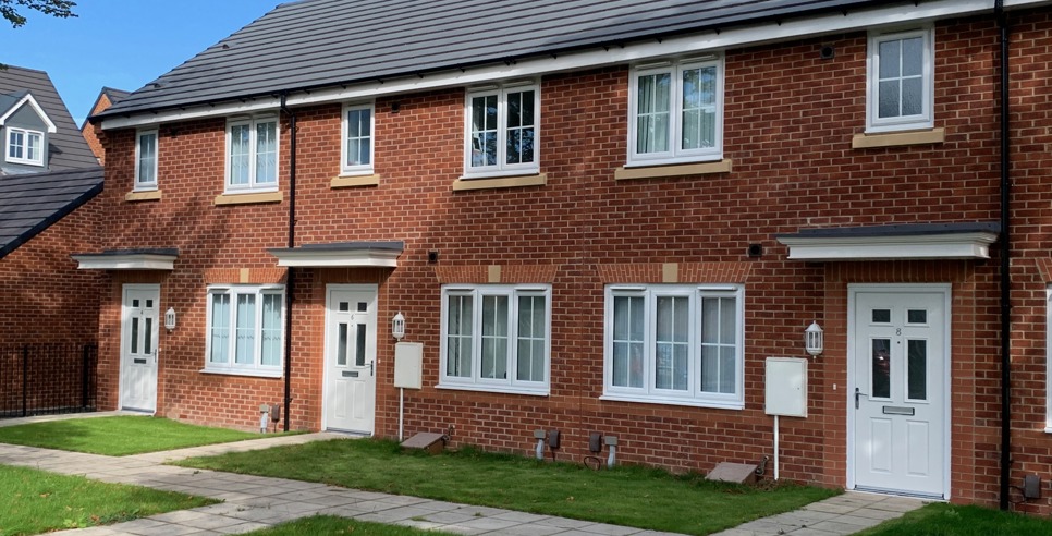 Red brick terraced houses with white windows and doors and a small front garden.
