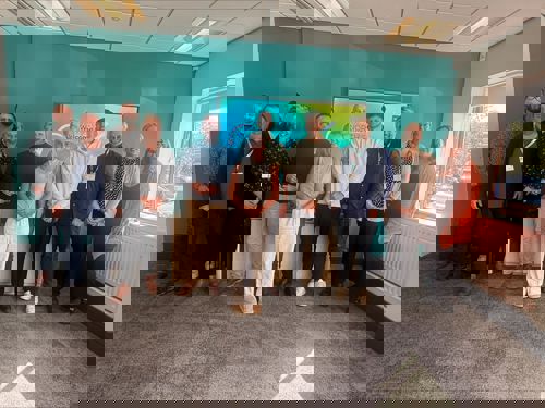 A group of people stood in a bright office boardroom smiling.