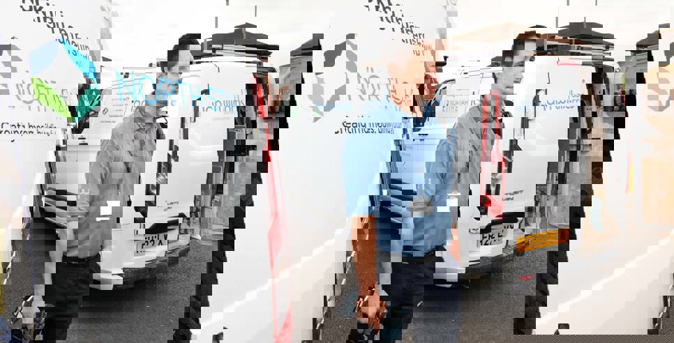 A repair worker stands between two branded vans from Ian Williams and North Star Housing. He is holding tools and wearing a blue uniform and lanyard. The vans display the logos and partnership between Ian Williams and North Star Housing.