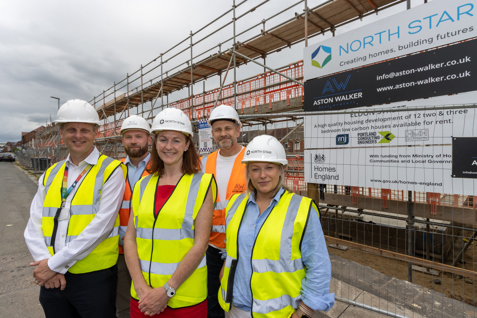 Group of people wearing hi vis vests and hard hats stand outside live construction site