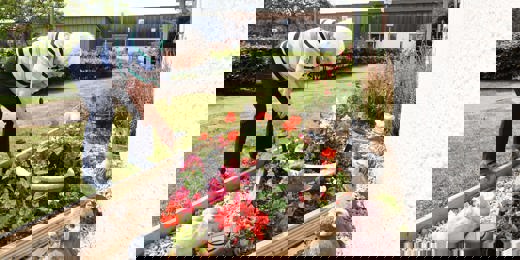 A woman tends to a flower bed surrounded by flowers and garden ornaments.