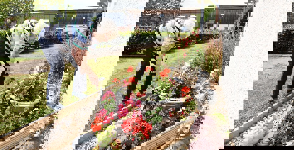 A woman tends to a flower bed surrounded by flowers and garden ornaments.