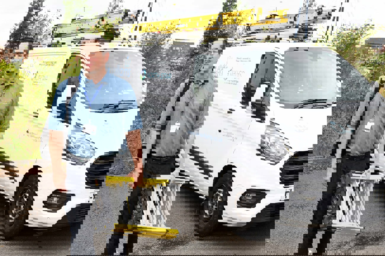 A maintenance worker from Ian Williams, carrying a ladder and a tool bag, stands beside a branded service van. The van features logos for Ian Williams and North Star Housing Group, highlighting their partnership.