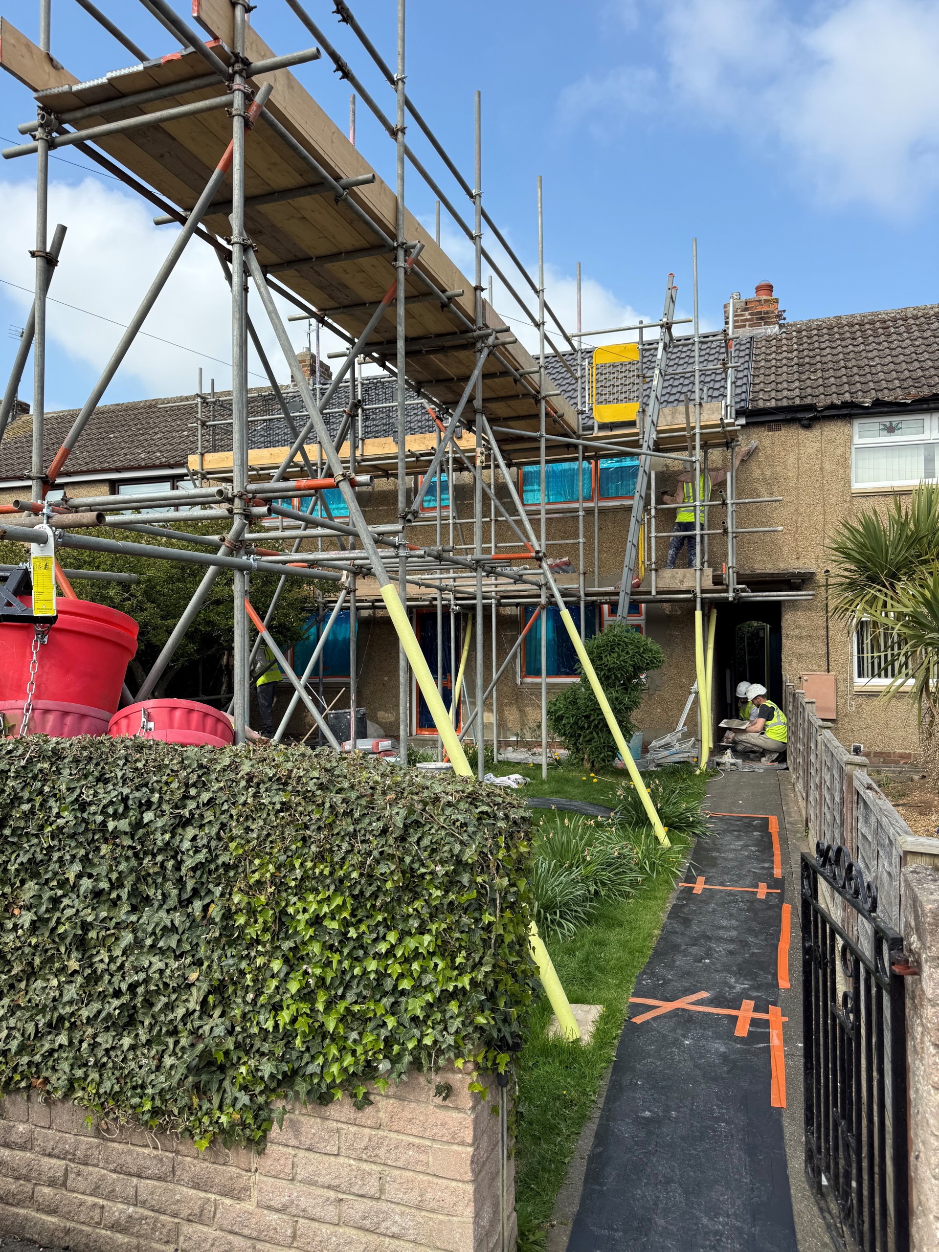 A terraced house with scaffolding, men working outside with high-viz jackets on.