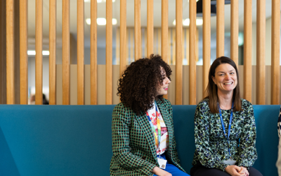 Four people sit on a bench in an open, modern office.