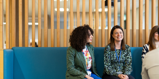 Four people sit on a bench in an open, modern office.
