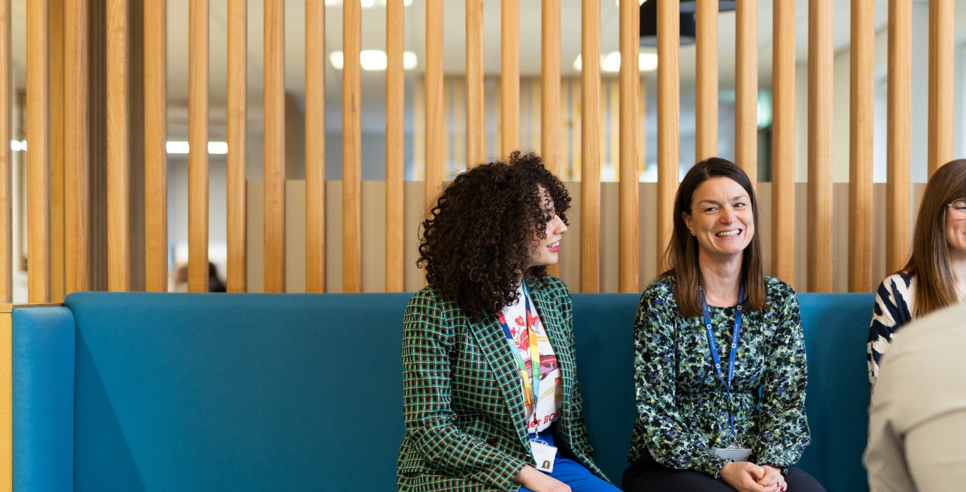 Four people sit on a bench in an open, modern office.