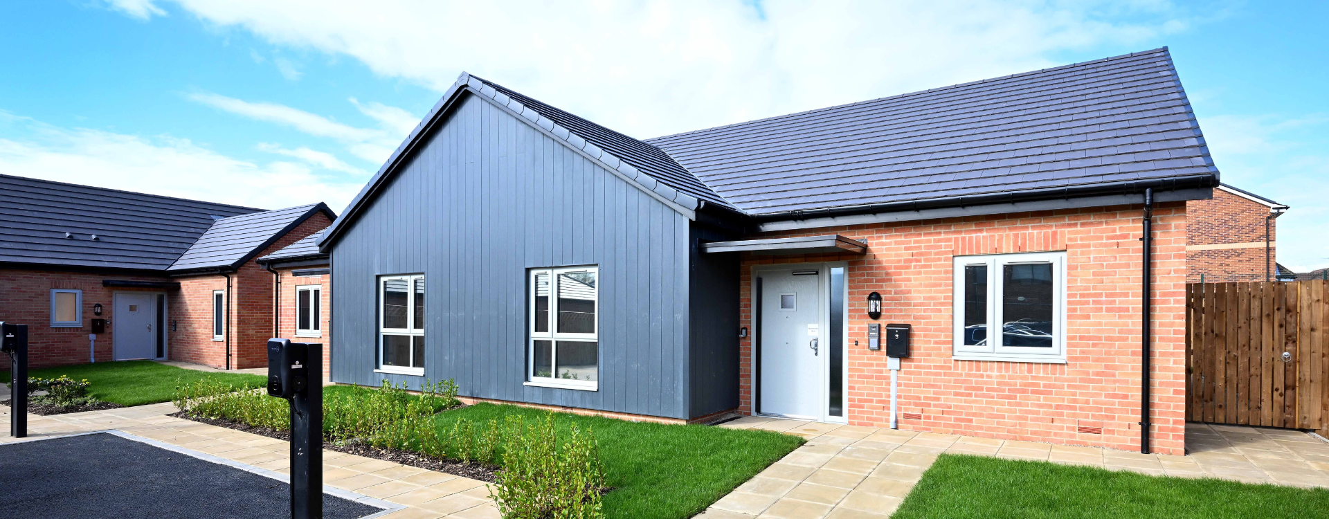 A newly built one storey home with red bricks, dark grey wooden panelling and a dark grey tiled roof.