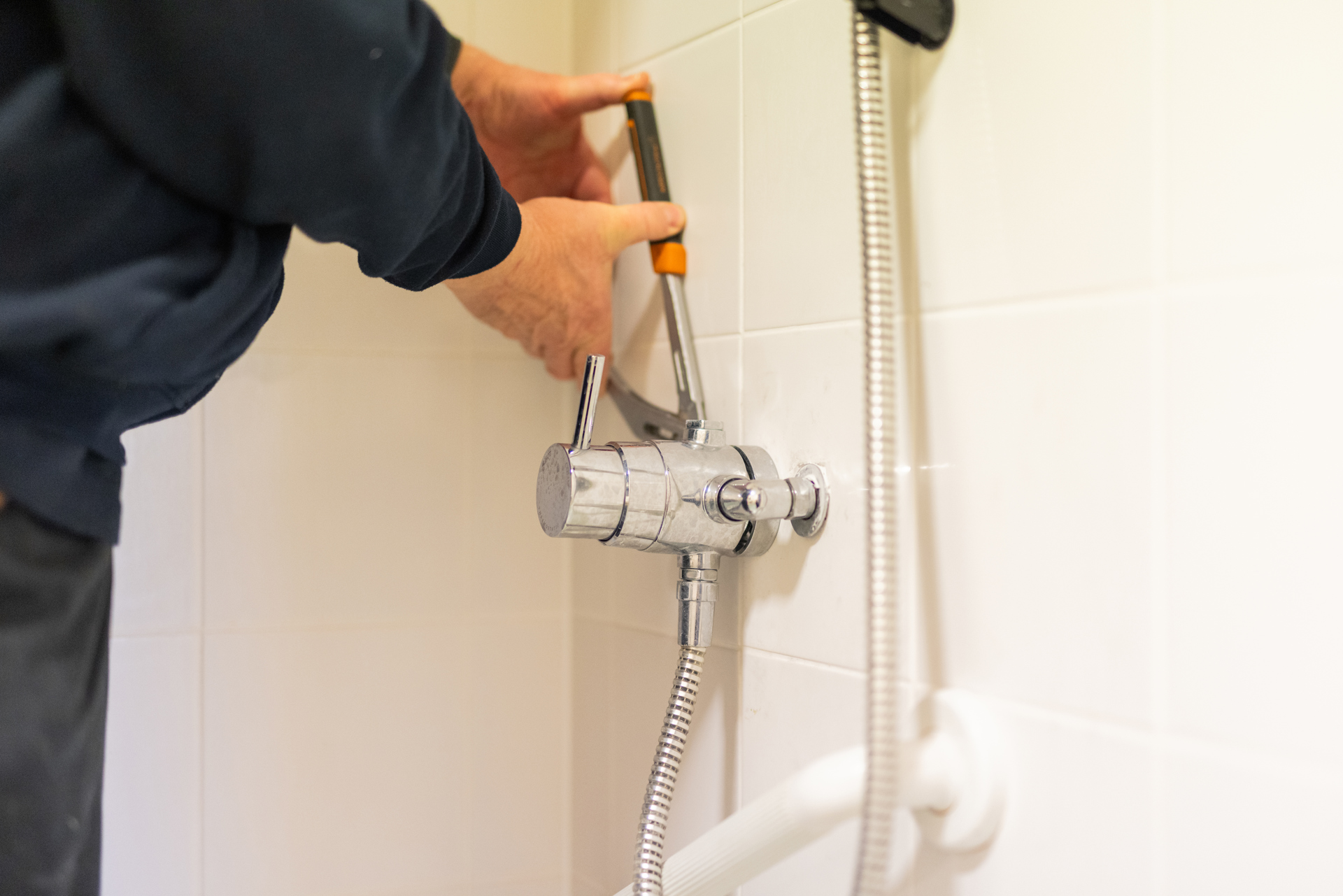 A person using tools to repair a shower tap.