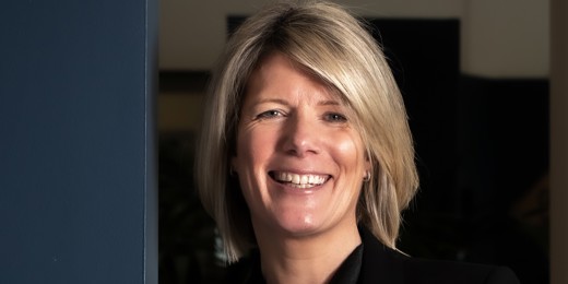 A woman in professional clothing smiles with her arms folded.
